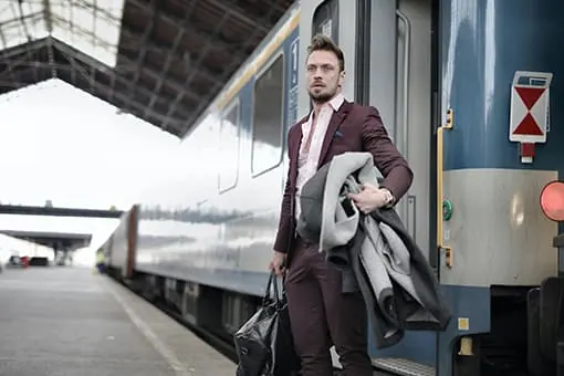 Un homme en costume avec un sac et un manteau se tient sur le quai près d’un train.