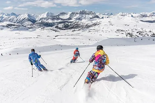 Trois skieurs descendent une piste dans un paysage alpin enneigé.